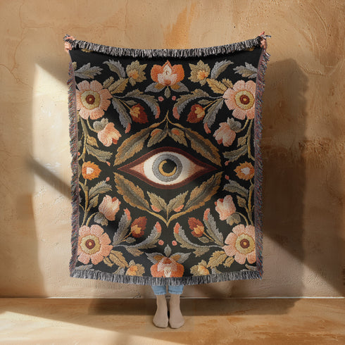 A luxury woven jacquard blanket in three sizes featuring an all-over wild herb botanical pattern of stylized blossoms and foliage in muted gold, olive, lavender, and pewter on a deep black cotton ground; finely twisted multicolor fringe edges complete the artful tapestry weave, ideal as a cozy sofa throw or dramatic wall hanging.